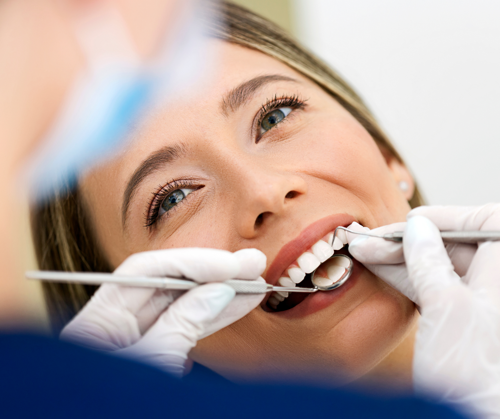 Woman at dentist smiling, being examined with tools and mirror.