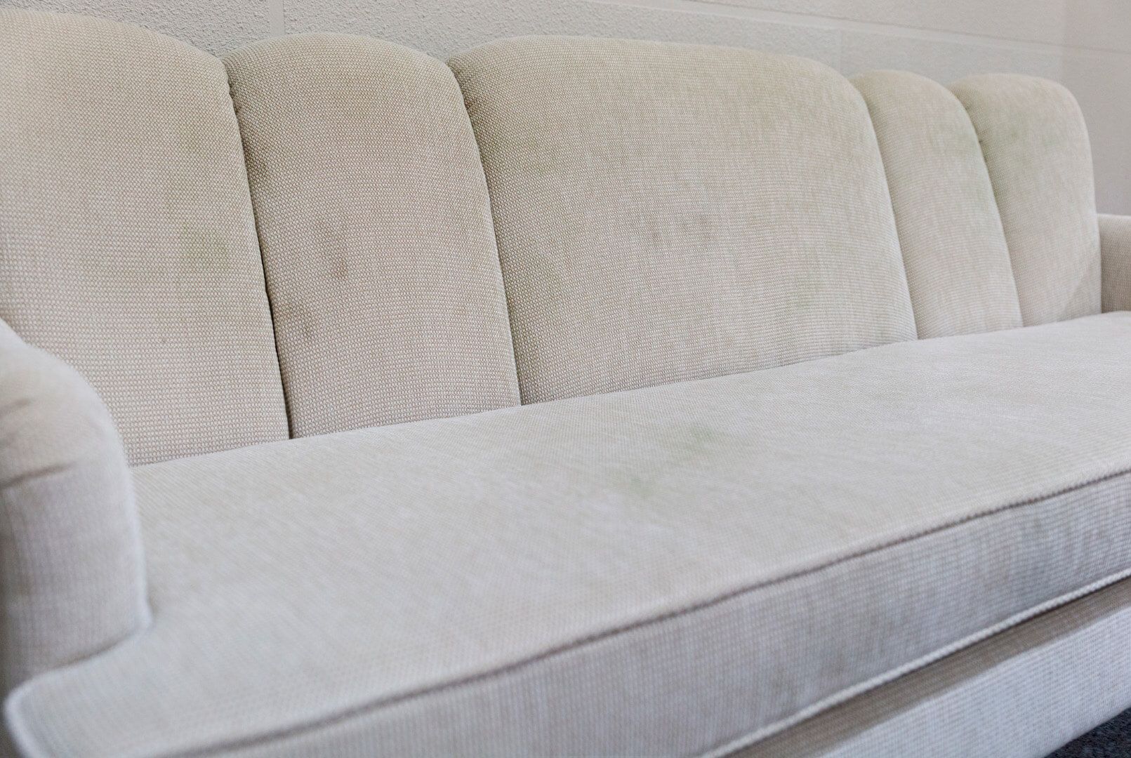 Sofá de tela texturizada en tonos neutros con paneles cosidos verticalmente en el respaldo.