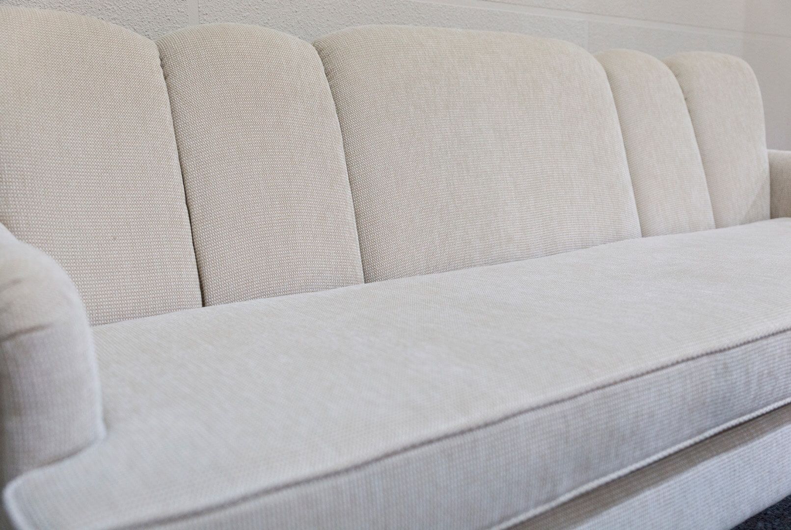 Un sofá de tela color beige claro con cinco paneles traseros acolchados verticales y un cojín de asiento liso y continuo.