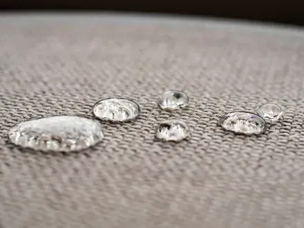 Water droplets sitting on a textured, light beige fabric, demonstrating water-repellent properties.