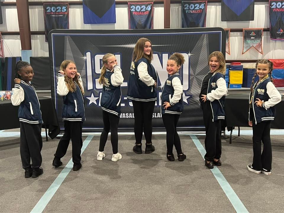Cheerleading team in navy and white jackets pose in front of a banner at an event.
