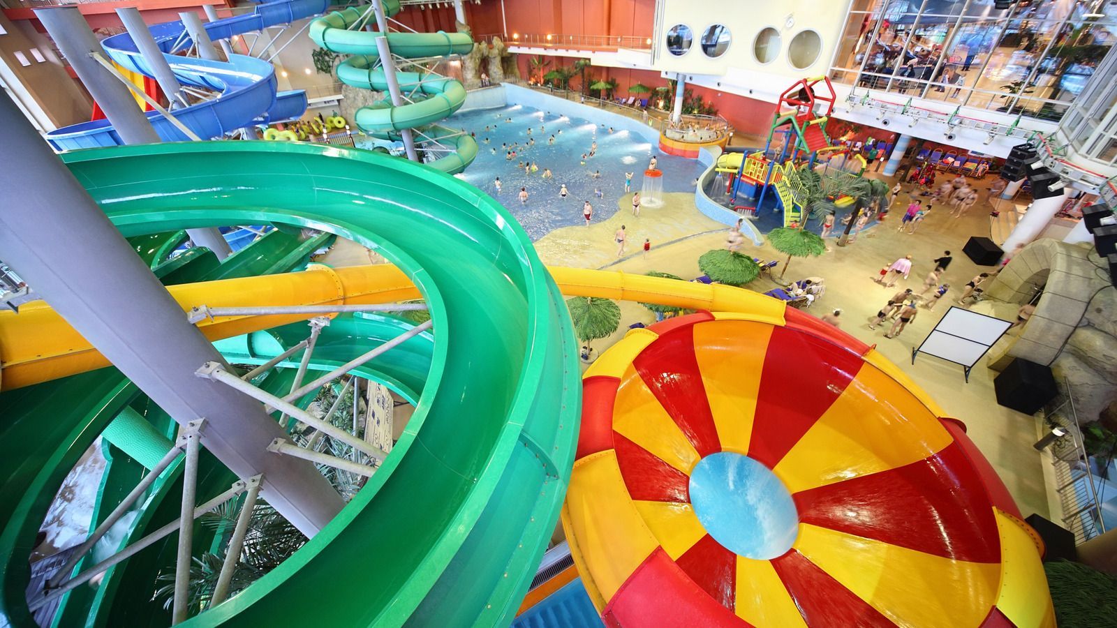 Indoor water park with multiple slides and a pool, vibrant colors, people enjoying the attractions.