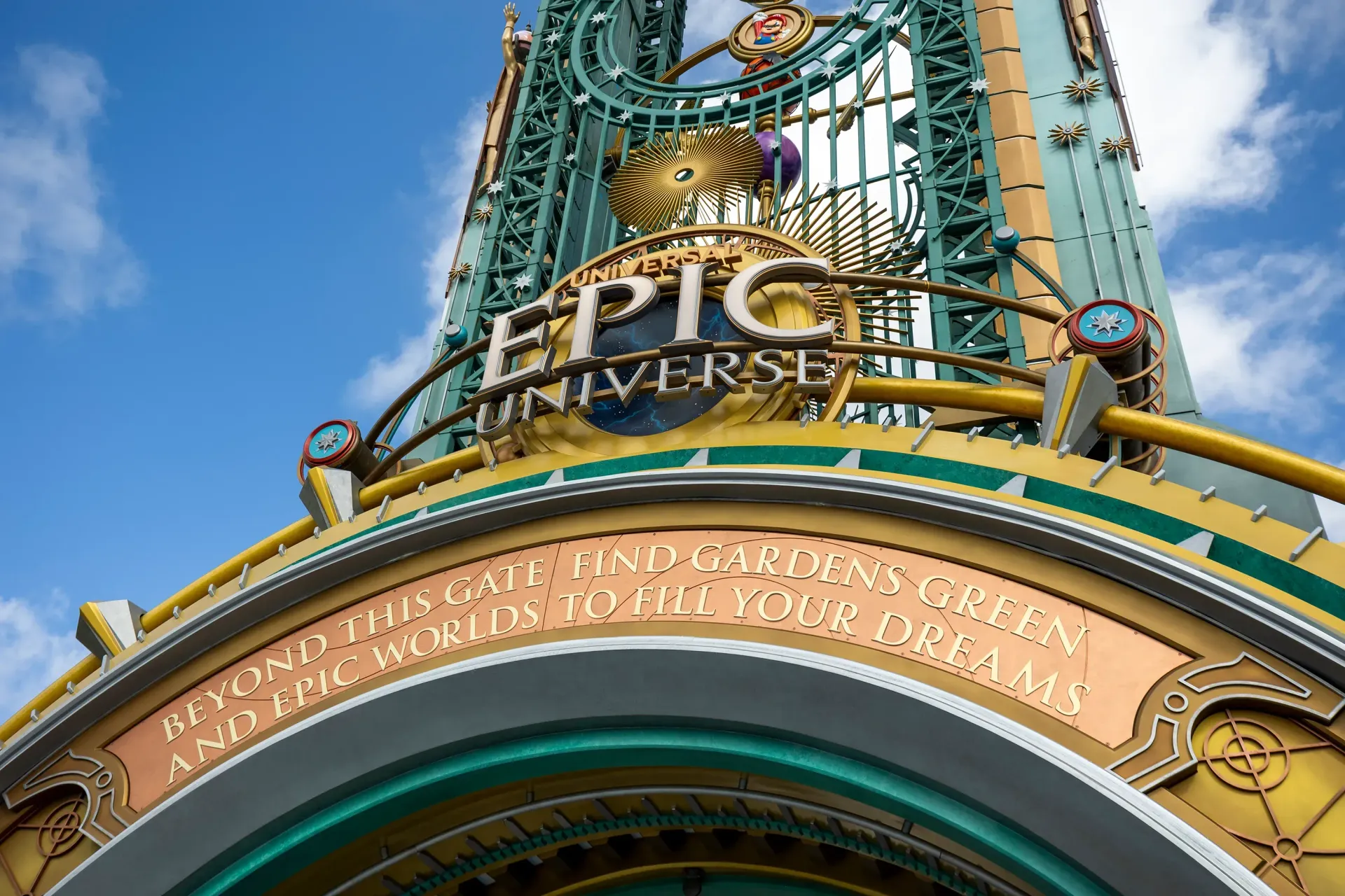 Epic Universe park entrance sign, turquoise and gold, with quote: 