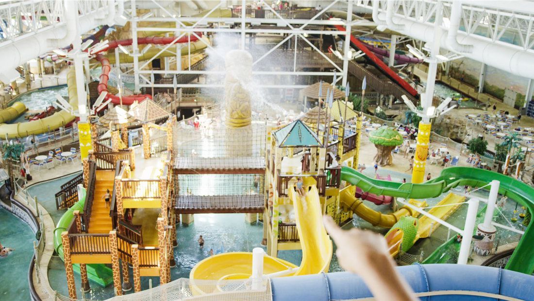Indoor water park with multiple waterslides and pools, seen from above. Bright and colorful with wooden structures.