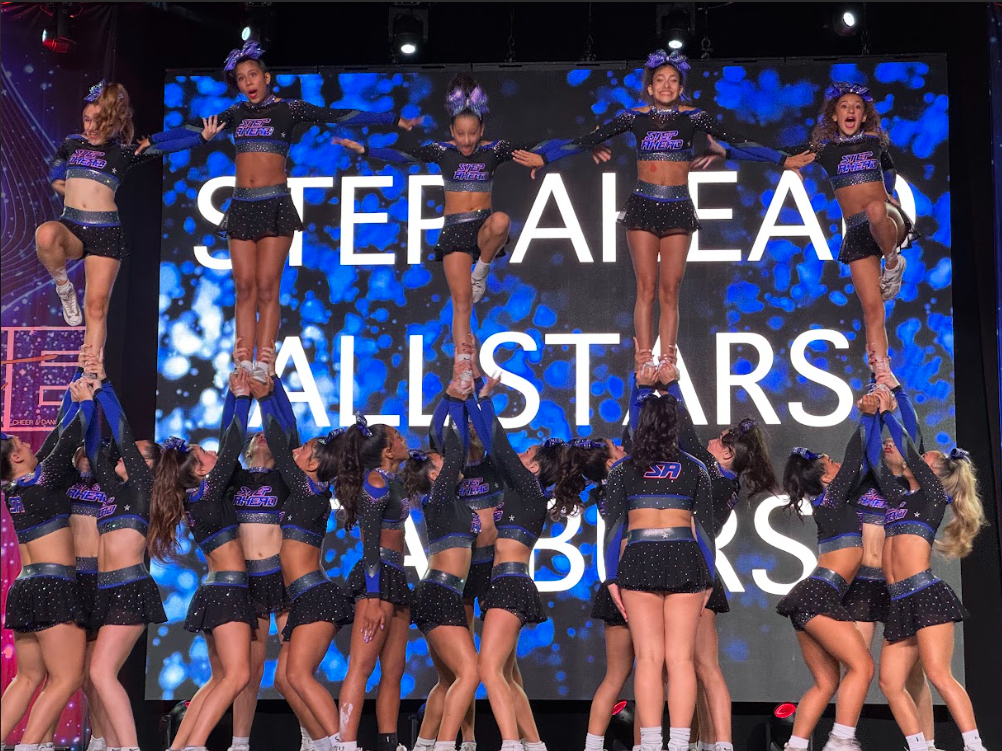 Cheerleaders in black and purple uniforms performing a stunt with a 