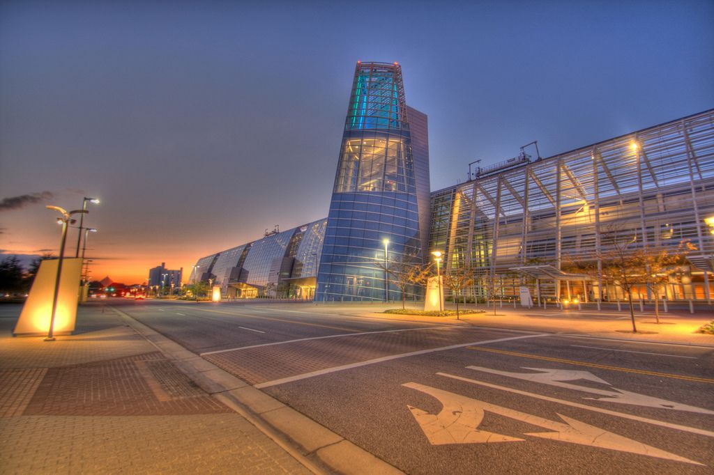 Modern building with blue and glass facade at dusk, illuminated street and cloudy sky.