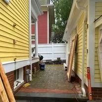 Narrow alley between two yellow buildings. Stone ground with white fence and red brick building in the distance.
