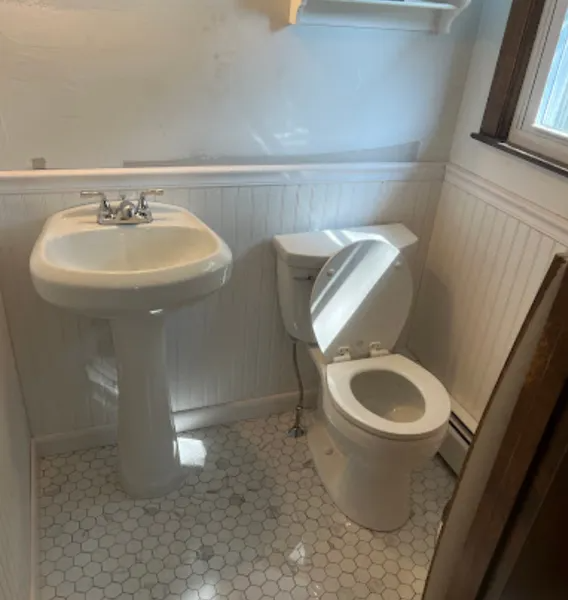A small bathroom with pedestal sink and toilet. White walls and hexagon tile floor.