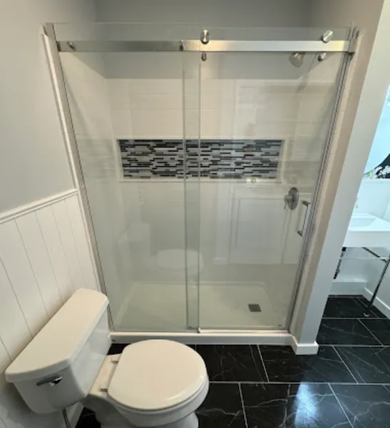 Bathroom with a glass sliding door shower, toilet, and black tile floor.