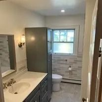 Bathroom with a toilet, vanity, and a tall cabinet. The walls are tiled, and there's a window.
