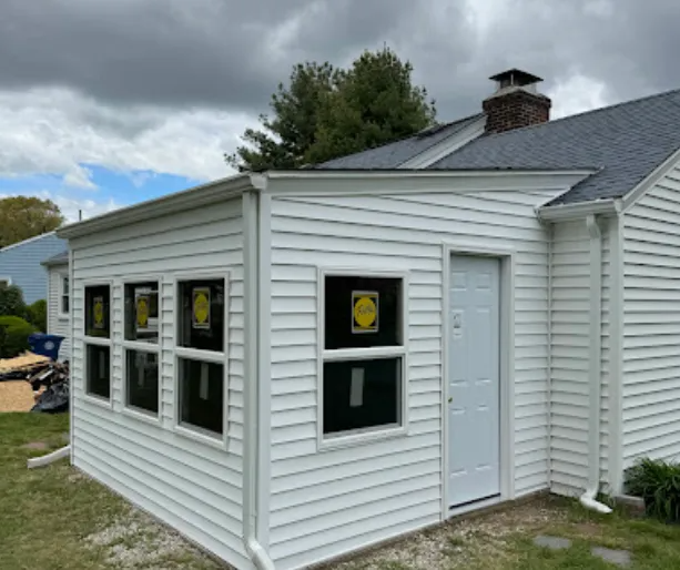White-sided addition on a house with several windows and a door under a gray sky.