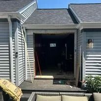 Open doorway into a dark interior under a house's gray roof and siding.