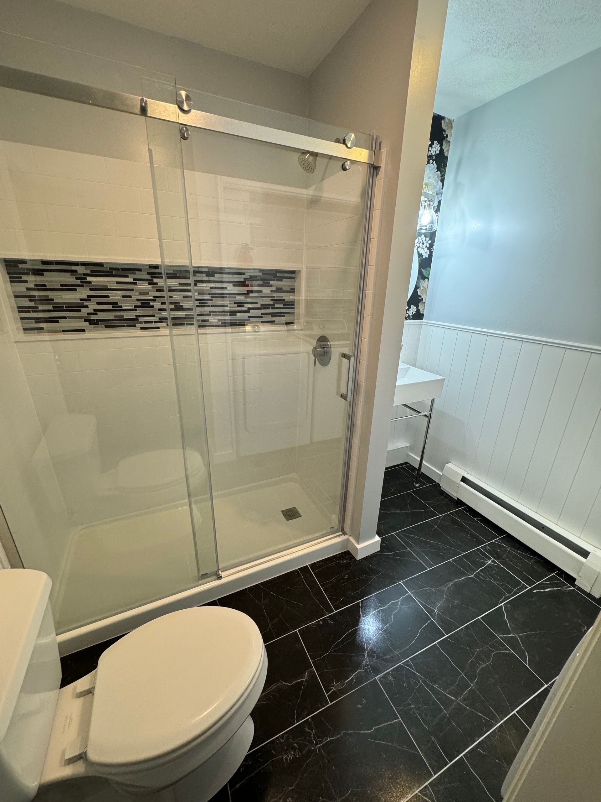 A small bathroom with pedestal sink and toilet. White walls and hexagon tile floor.