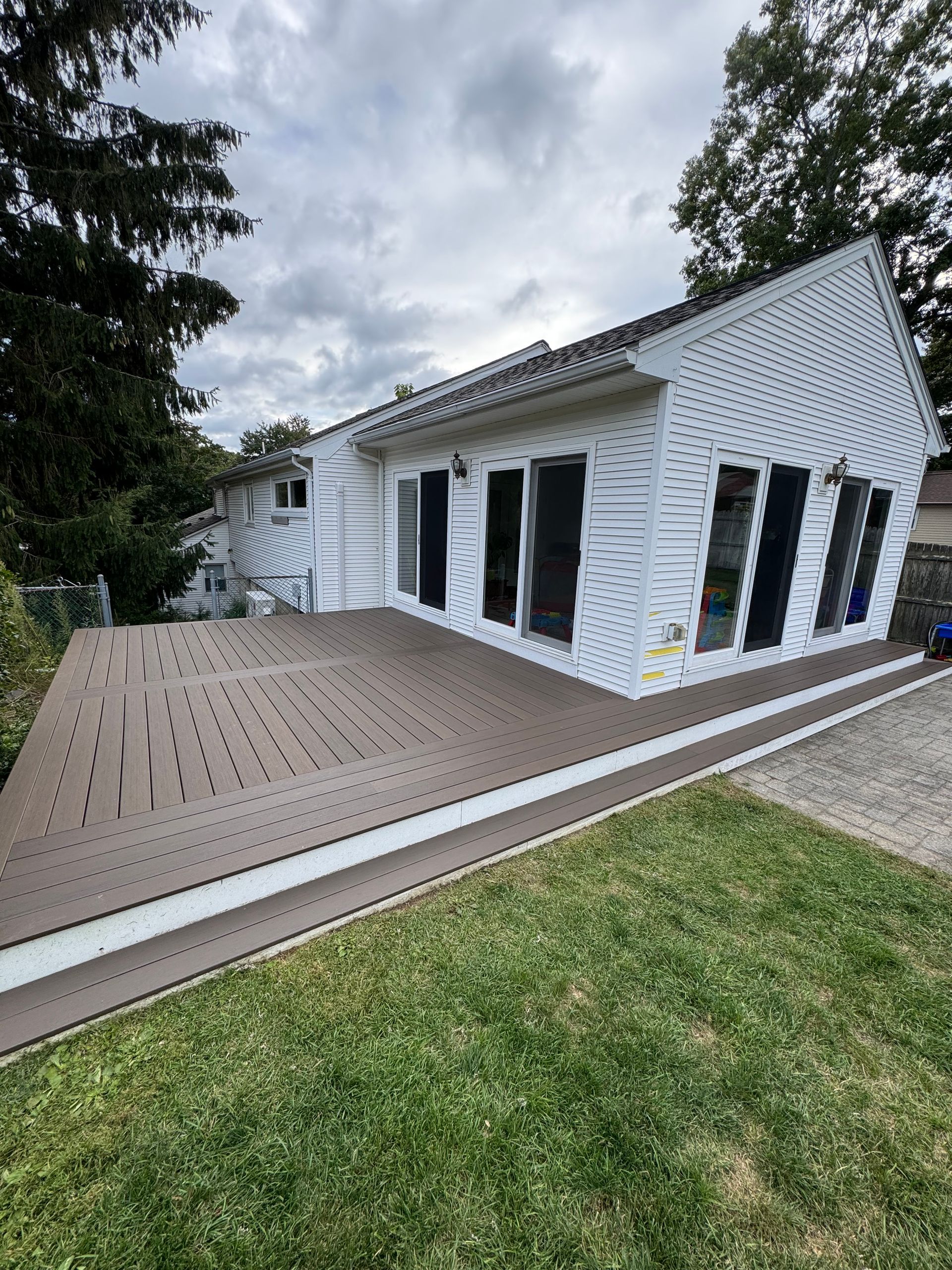 Wooden deck with outdoor furniture: table with umbrella, chairs, and armchairs on a lawn.