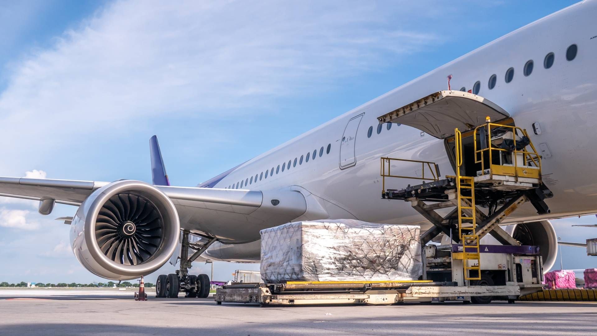 Cargo being loaded onto a commercial airplane at an airport, using a lift, under a blue sky.