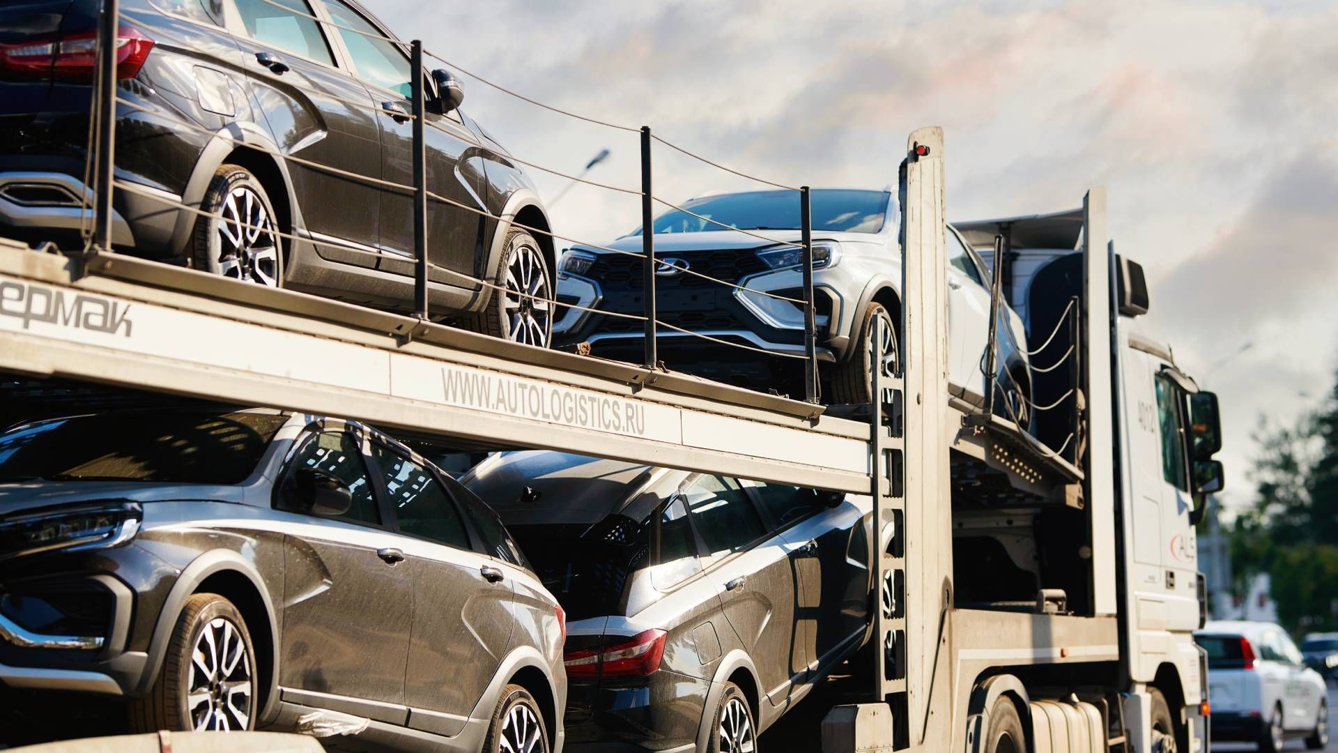 A car carrier truck transporting multiple new vehicles, mostly black and gray, on a cloudy day.