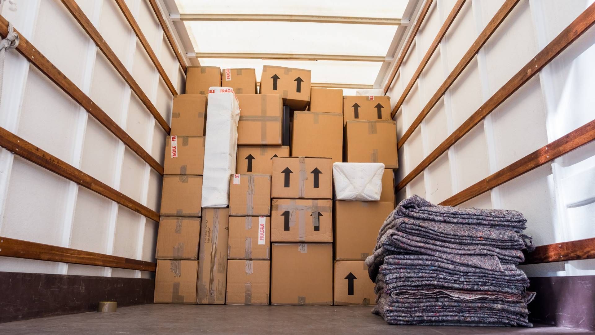 Boxes stacked inside a moving truck, with a pile of padding to the right.