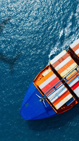 Cargo ship at sea with containers, blue hull, and ocean waves.
