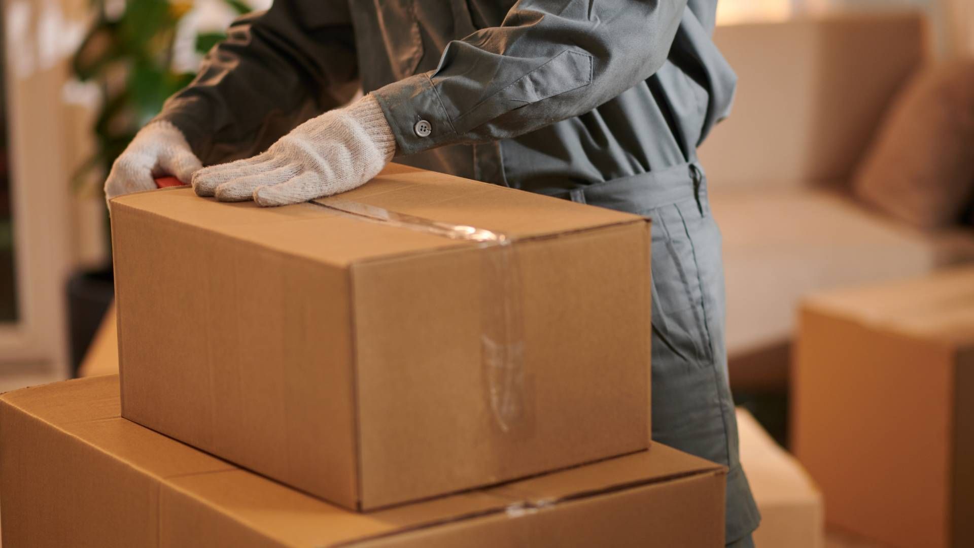 Person in work clothes and gloves sealing a cardboard box, stacked on another.