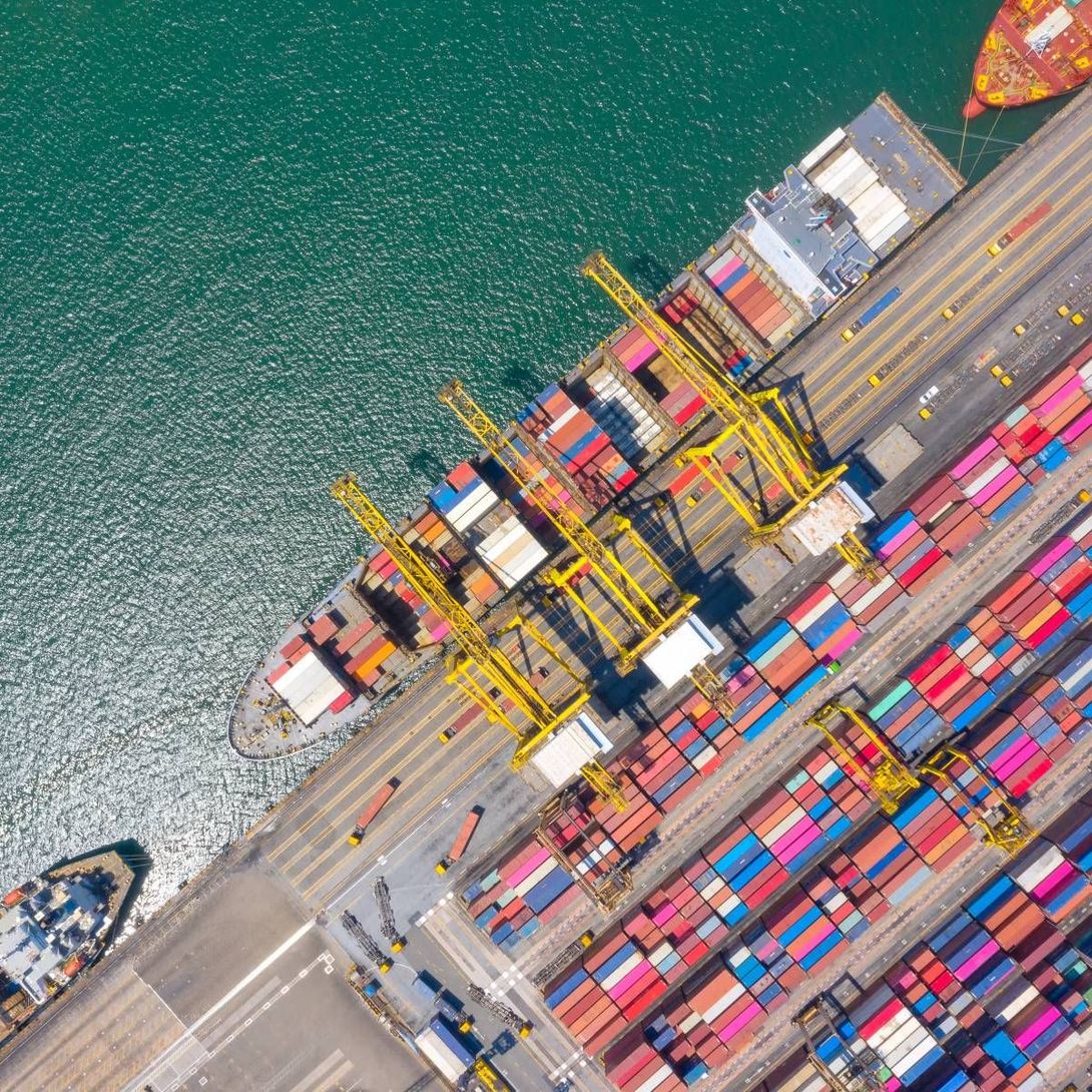 Aerial view of a port with a cargo ship, cranes, and colorful shipping containers.