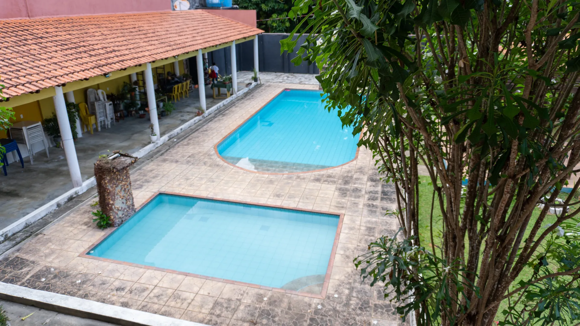 Duas piscinas e um pátio coberto. Uma árvore em primeiro plano - Solar Café e Pousada