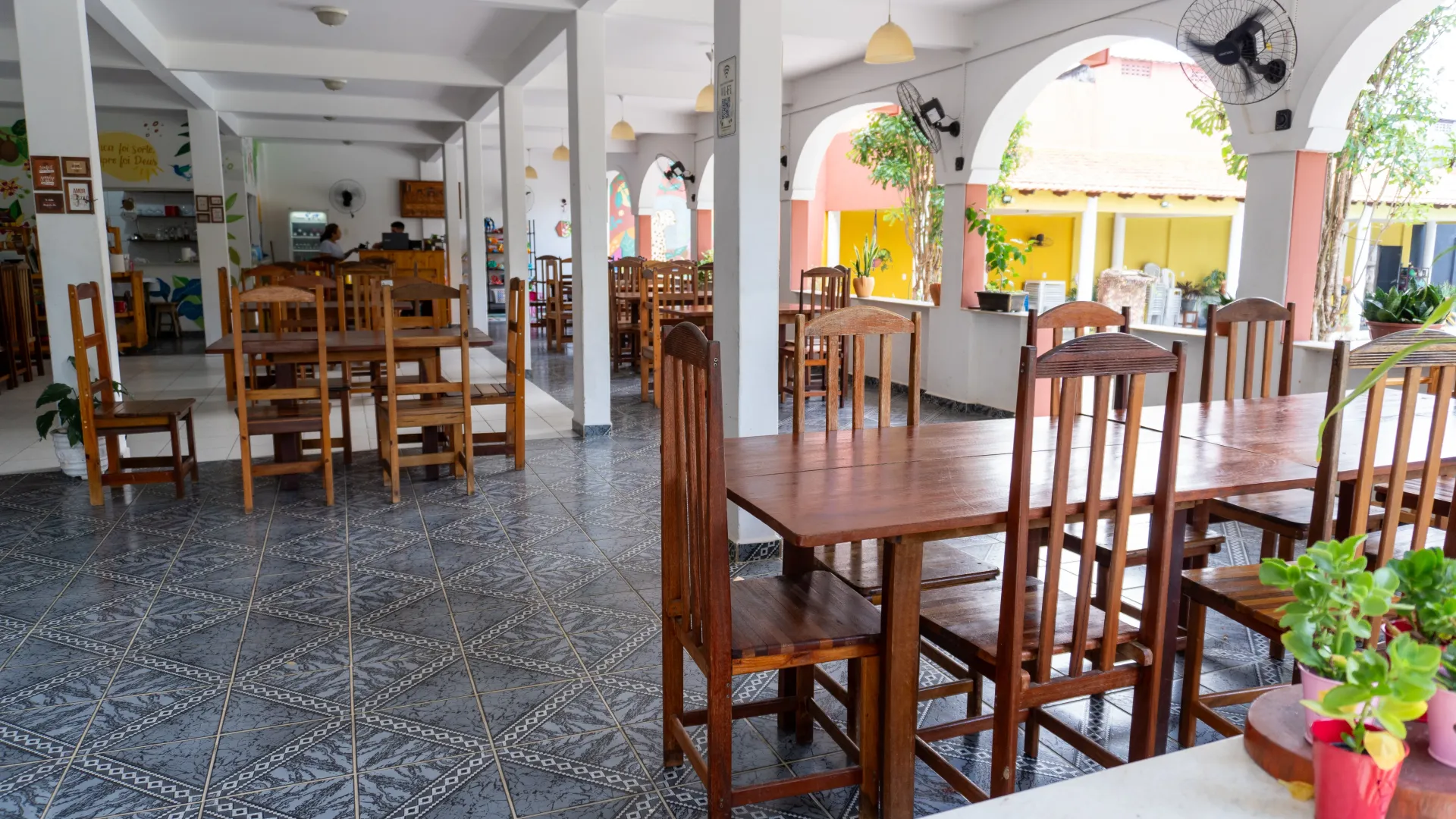 Área de jantar ao ar livre vazia com mesas e cadeiras de madeira sob um teto arqueado branco - Solar Café e Pousada