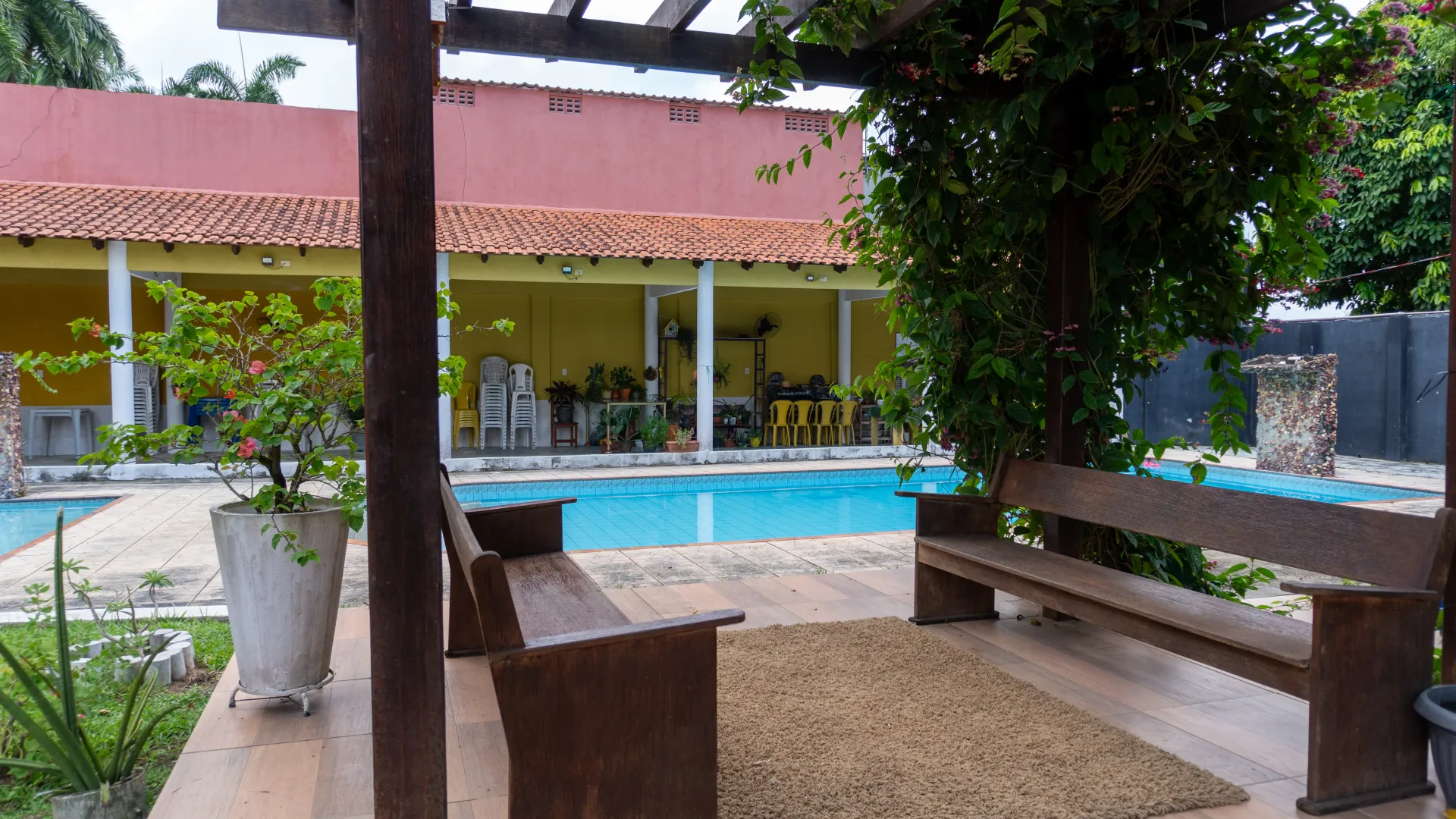 Pátio externo com piscina e um prédio com exterior amarelo - Solar Café e Pousada