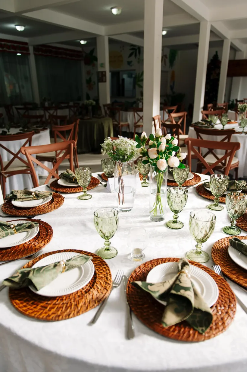 Elegante arranjo de mesa para um casamento. Mesa redonda branca com jogos americanos de tecido, centros de mesa florais e copos verdes - Solar Café e Pousada