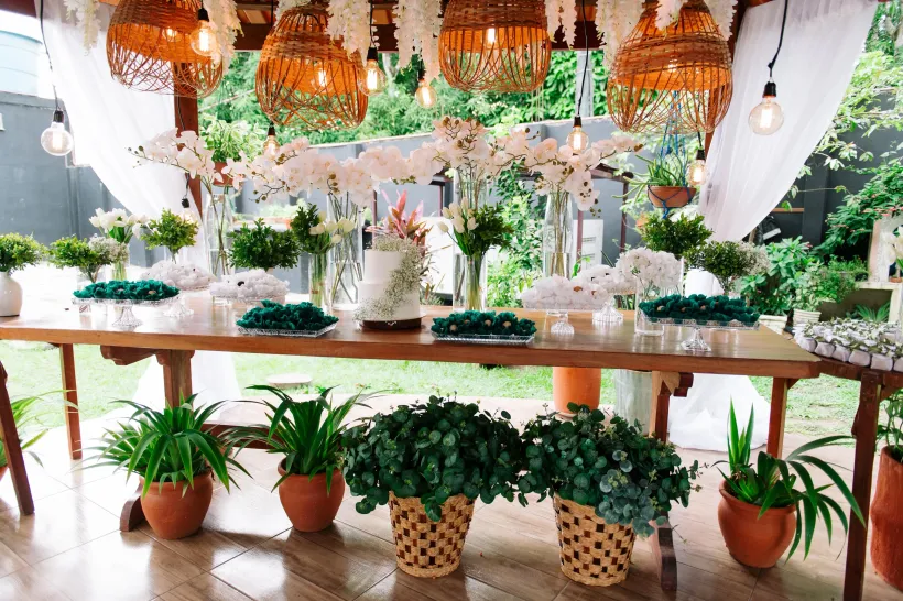 Uma mesa decorada para uma festa com flores, bolo e luzes penduradas; esquema de cores verde e branco, ambiente externo - Solar Café e Pousada