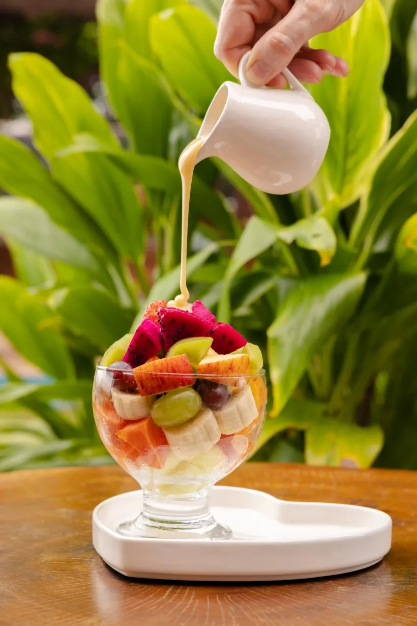 Salada de frutas em um prato de vidro, coberta com pitaia, regada com molho branco, em ambiente externo - Solar Café e Pousada