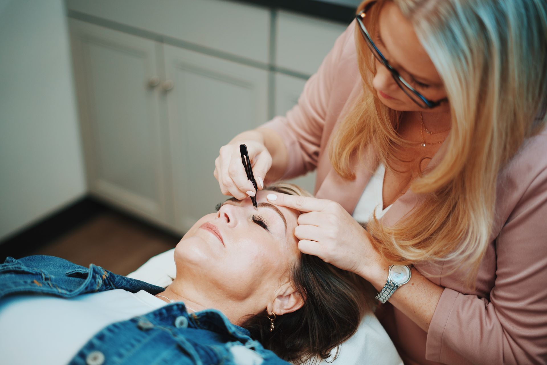 A woman is applying makeup to another woman 's eyebrows.
