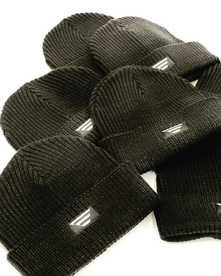 A bunch of black beanies are stacked on top of each other on a white surface.