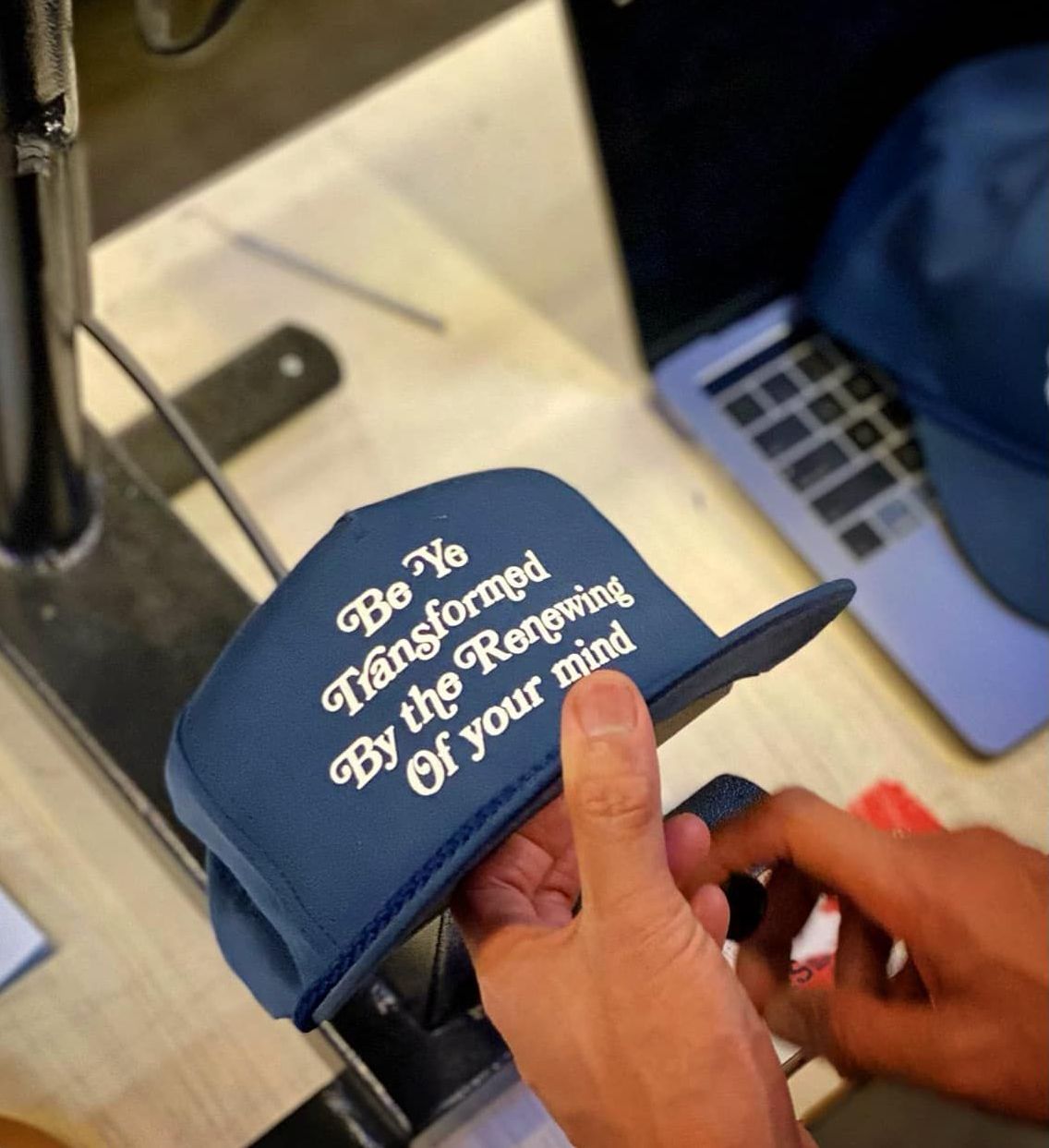 A person is holding a hat that says be ye transformed by the renewing of your mind