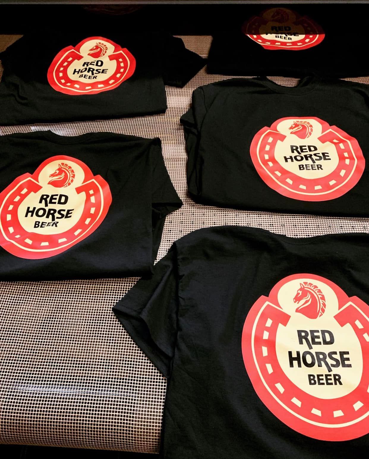 Several black t-shirts with red horse beer on them