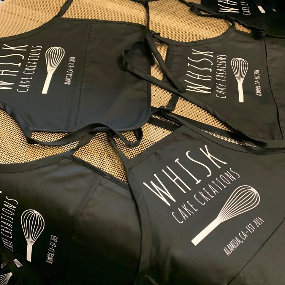 Three black aprons with whisk cake creations written on them
