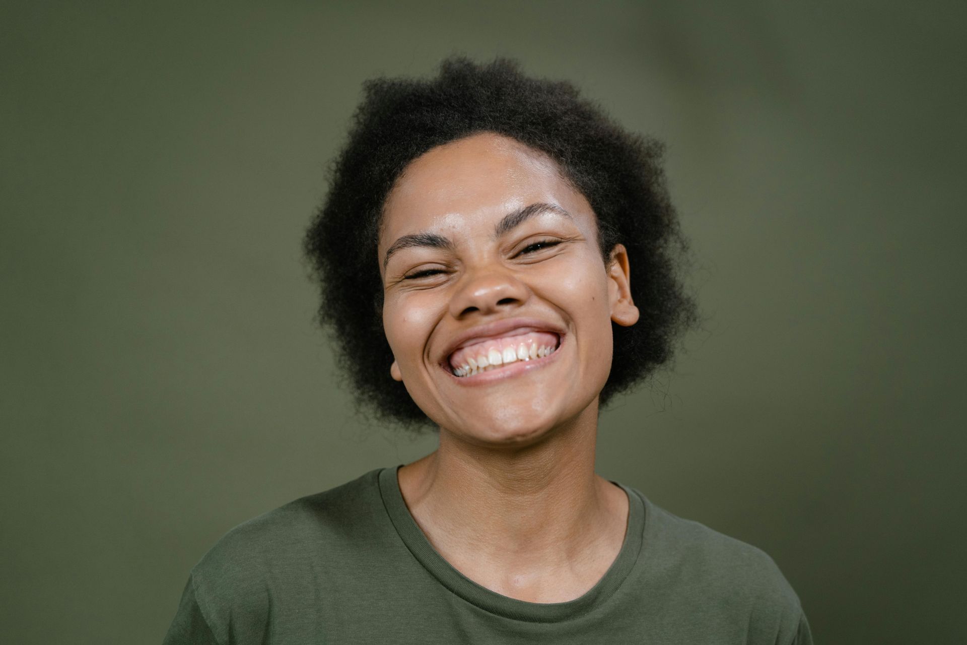 A woman in a green shirt is smiling with her eyes closed.