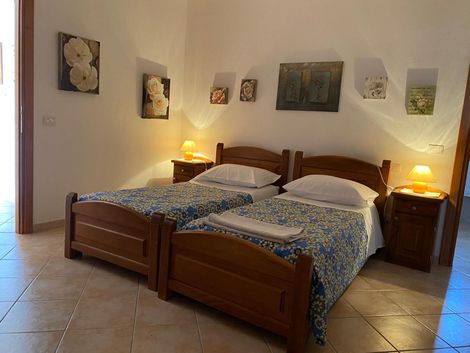 Accogliente camera da letto con due letti singoli in legno, lampade da comodino, quadri alle pareti e pavimento piastrellato.