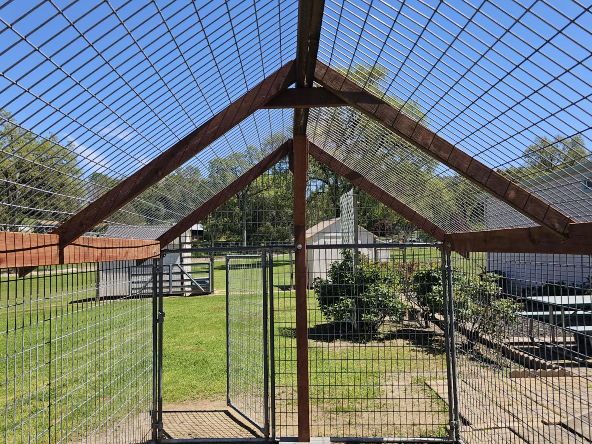 A dog kennel with a wooden roof and a metal fence