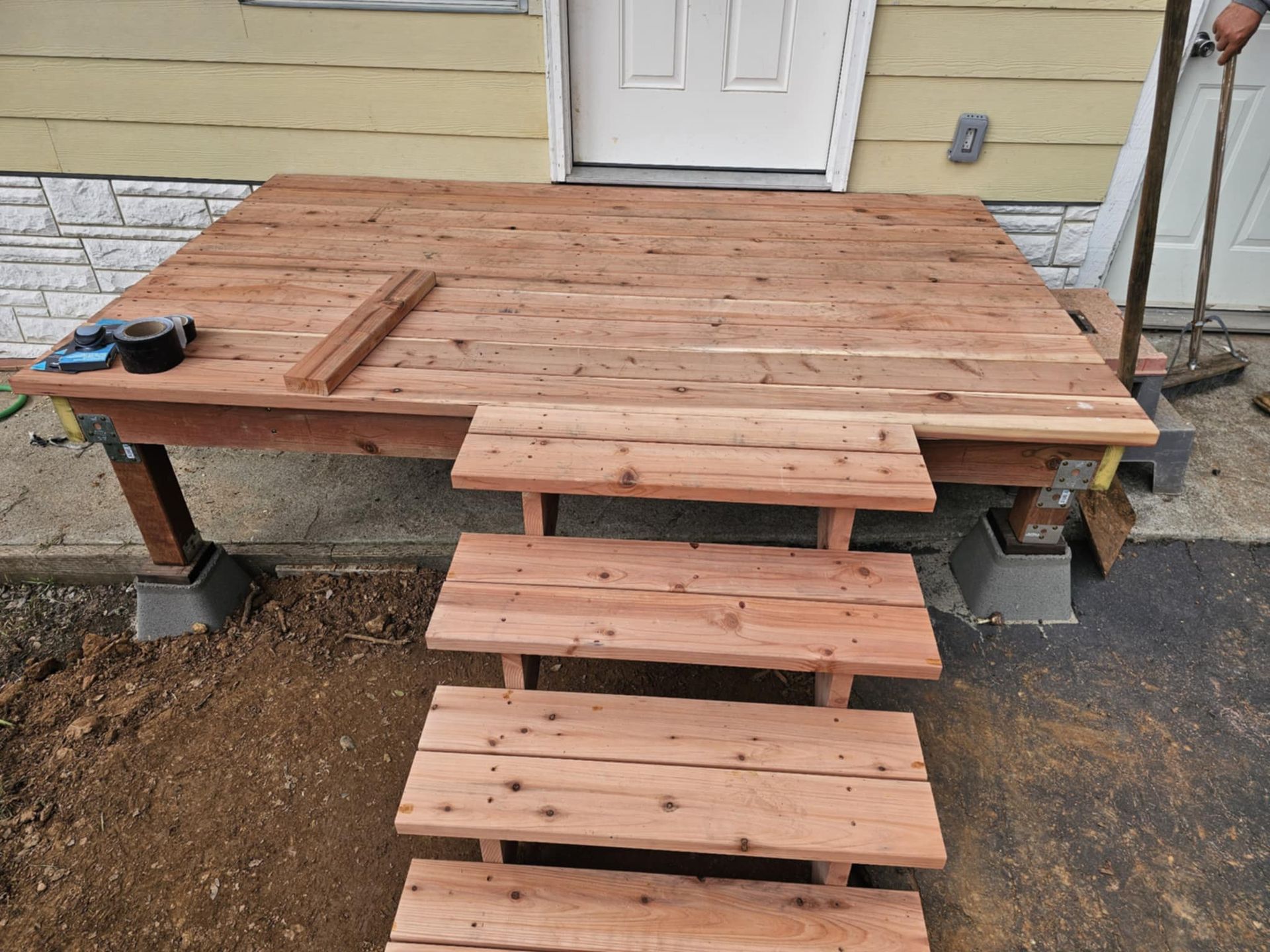 A wooden deck with stairs is being built in front of a house