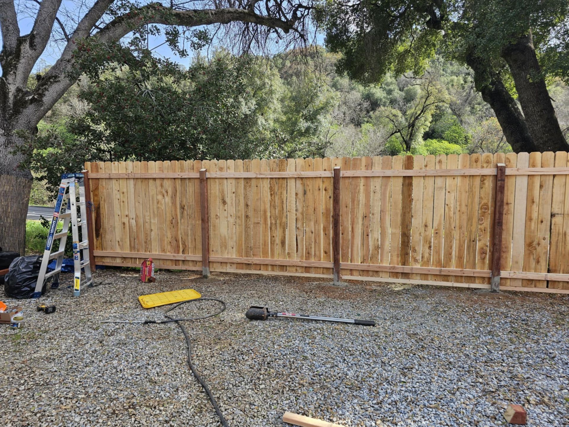 A wooden fence is being built in a gravel yard.