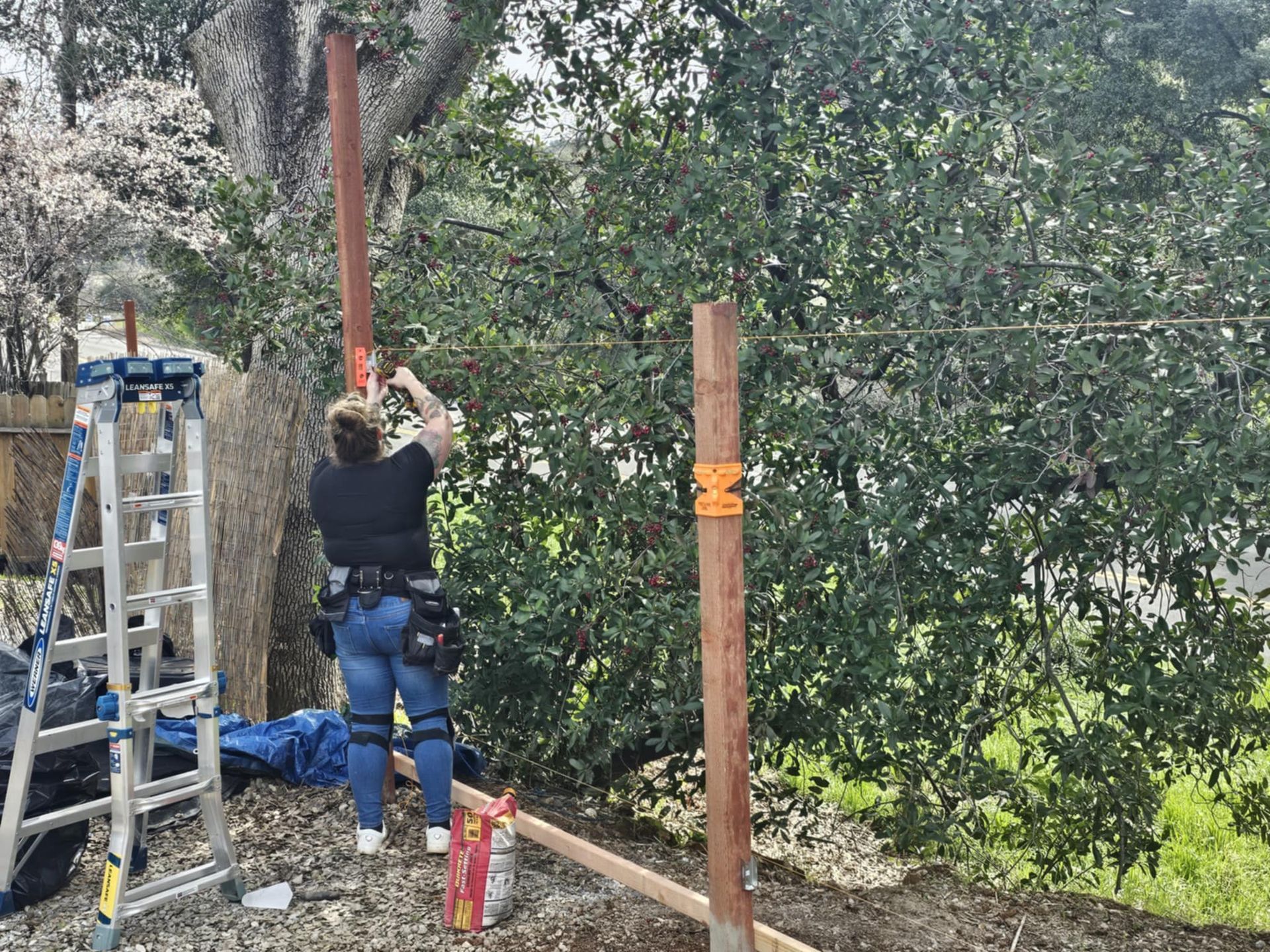A woman is standing next to a ladder and a wooden post.