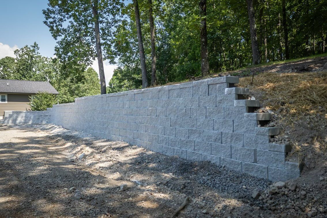 A long, gray, stepped concrete retaining wall under construction in a wooded residential yard.