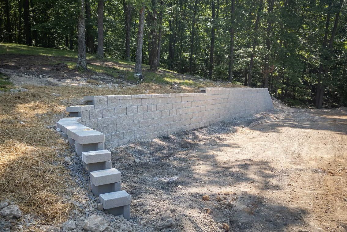 A light-colored stone retaining wall with integrated concrete steps, situated on a sloped site with trees in the background.