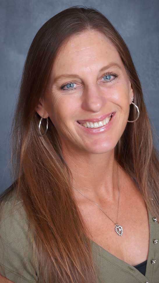 A woman is sitting at a desk with a laptop and a vase of flowers.