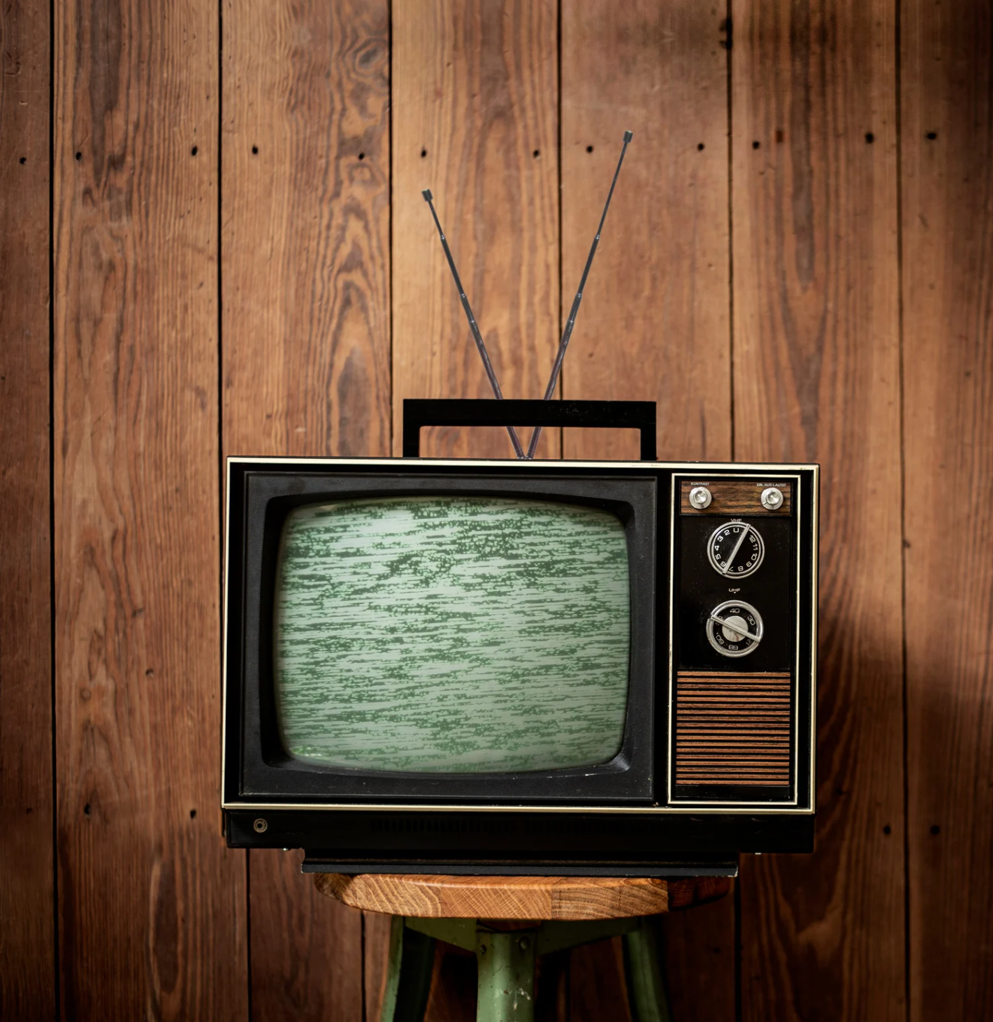 An old television is sitting on a stool in front of a wooden wall