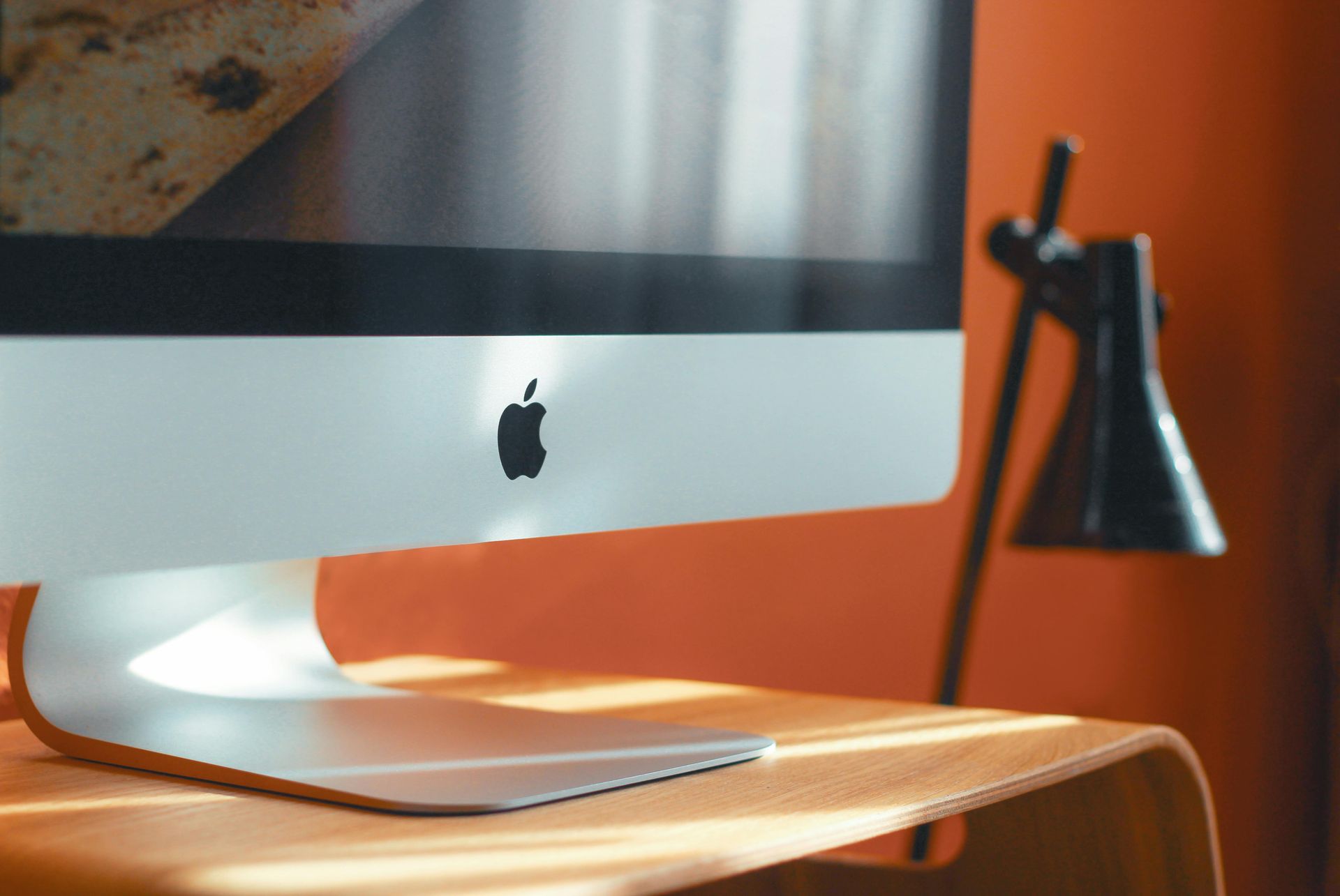 An apple computer is sitting on a wooden desk next to a lamp.
