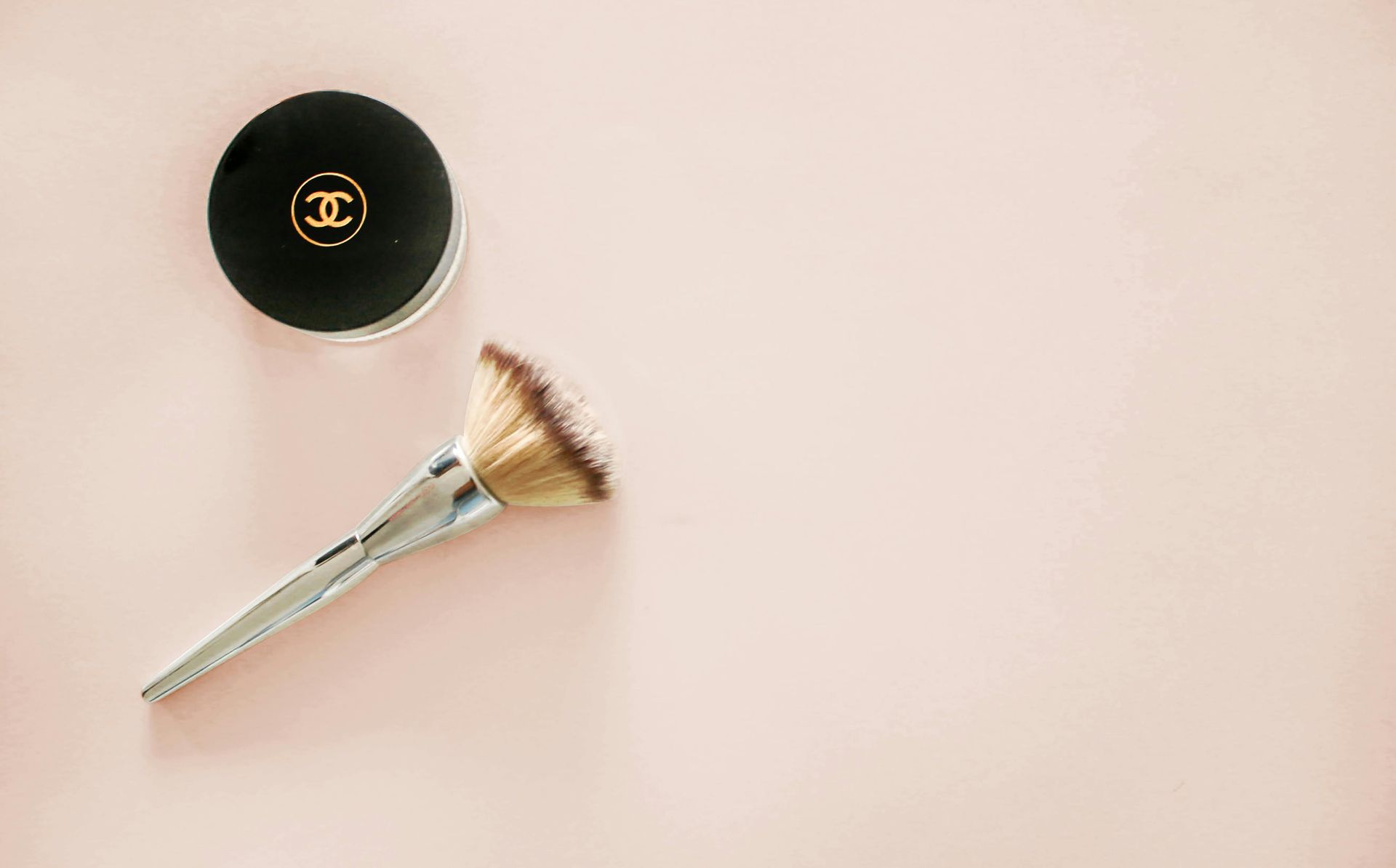 A brush and a container of powder are on a pink surface.