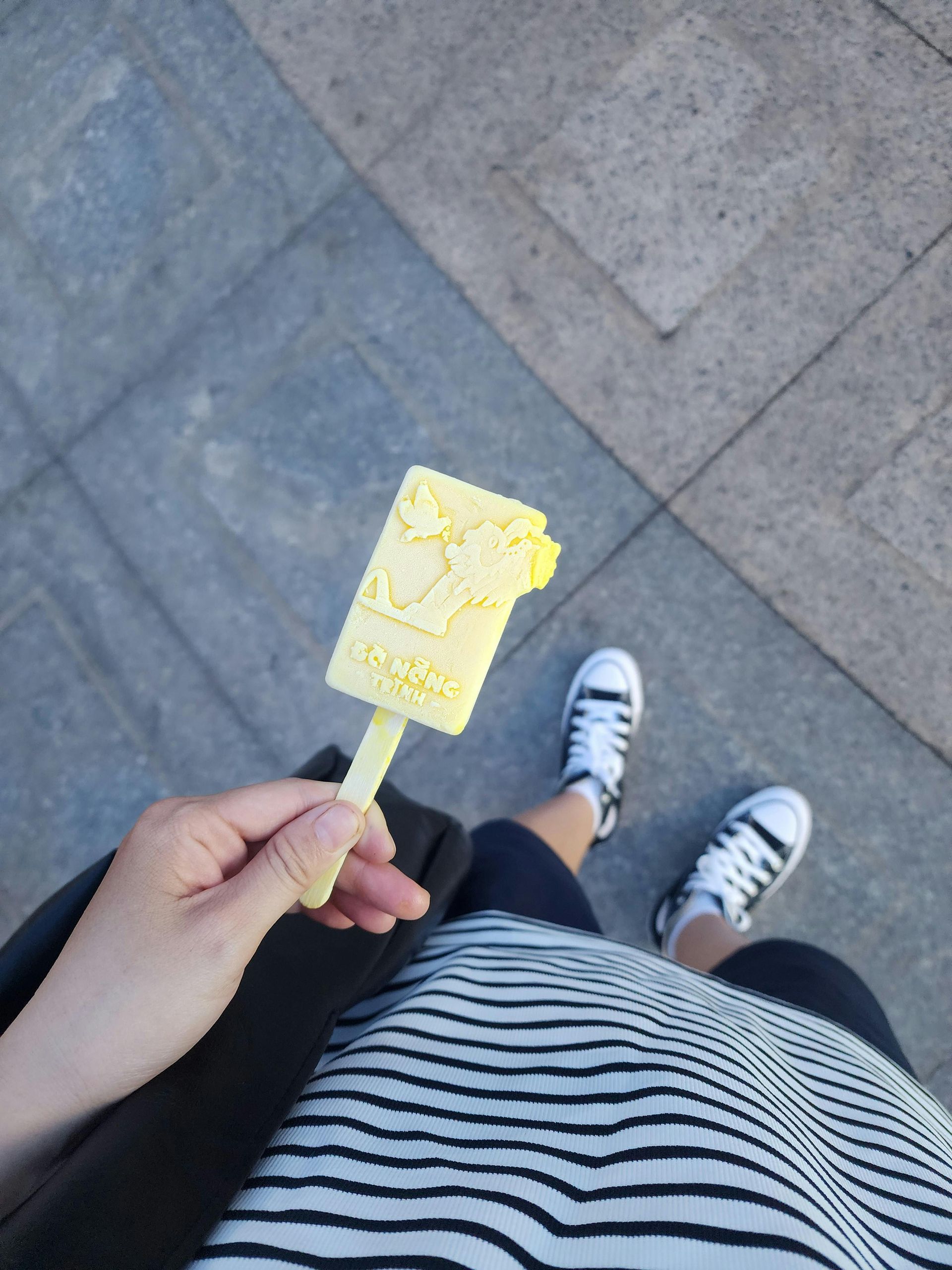 A person is holding a yellow popsicle in their hand