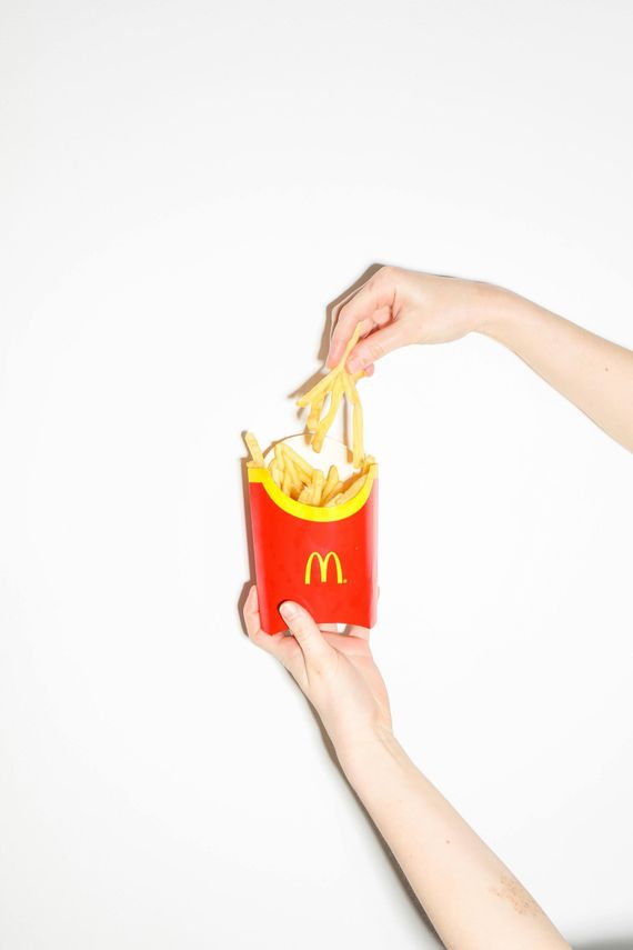 Two hands holding a red McDonald's fry box with fries spilling out against a white background.