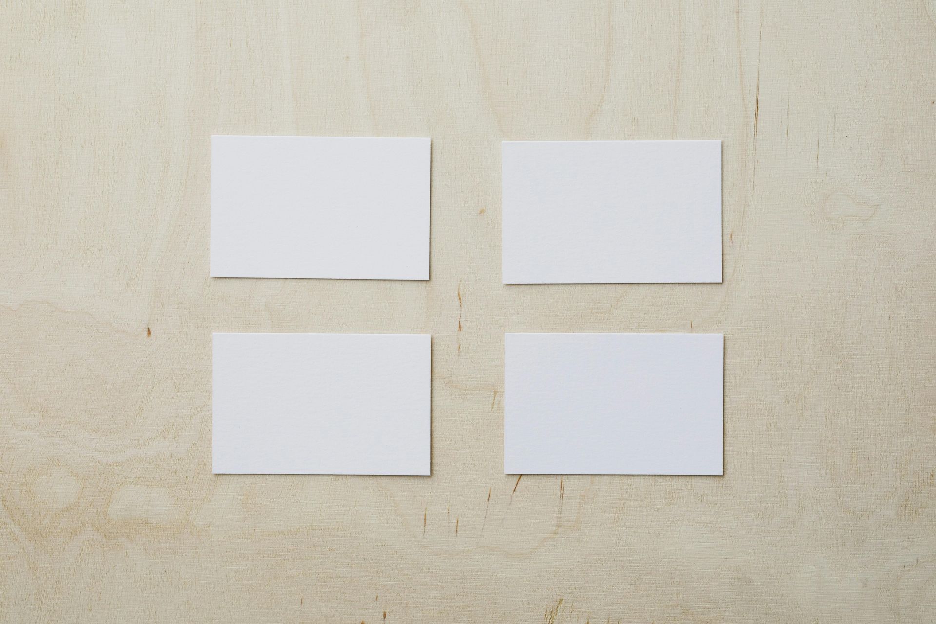 Four white business cards are stacked on top of each other on a wooden table.
